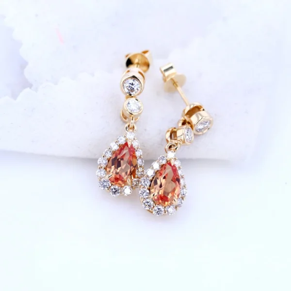"Elevate your style with the AMIIZE Gold Filled Earrings, featuring a stunning pear-cut orange sapphire set in a 14k gold filled halo setting. - Image 2